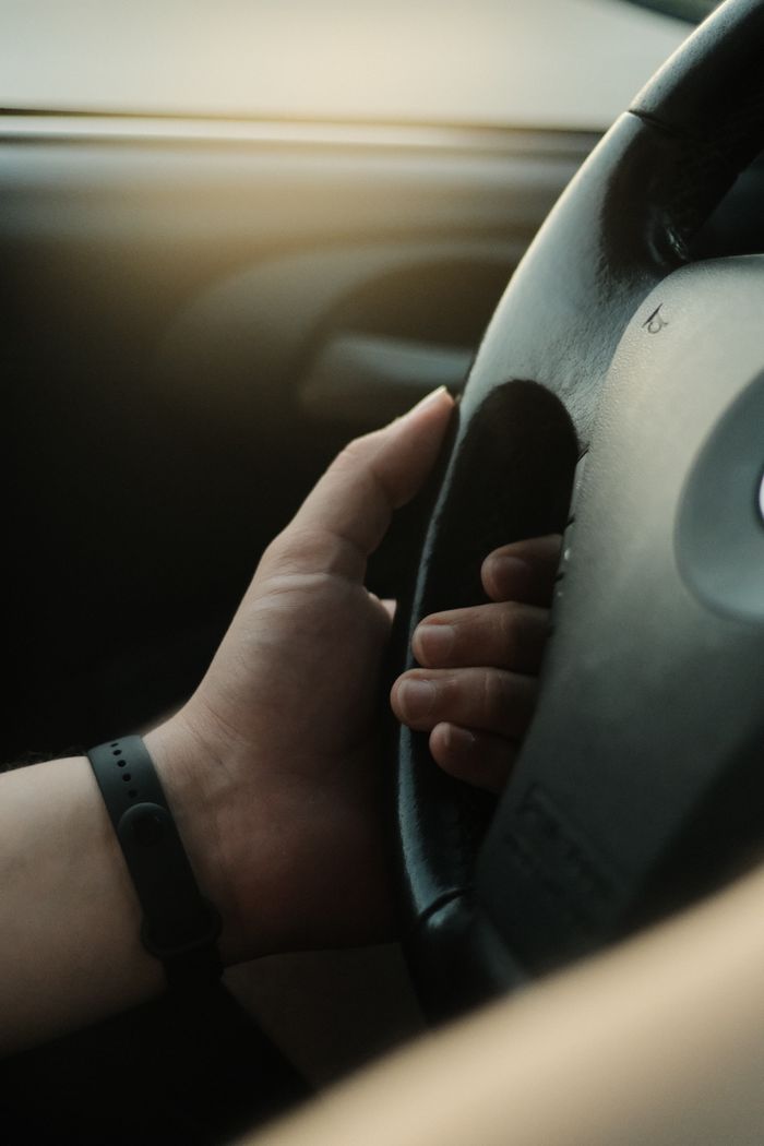 Close-up view of a hand holding a steering wheel inside a car, soft morning light enhancing the scene.