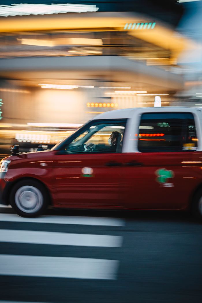 Dynamic shot of a red taxi driving through a city at night, showcasing urban motion and city life.
